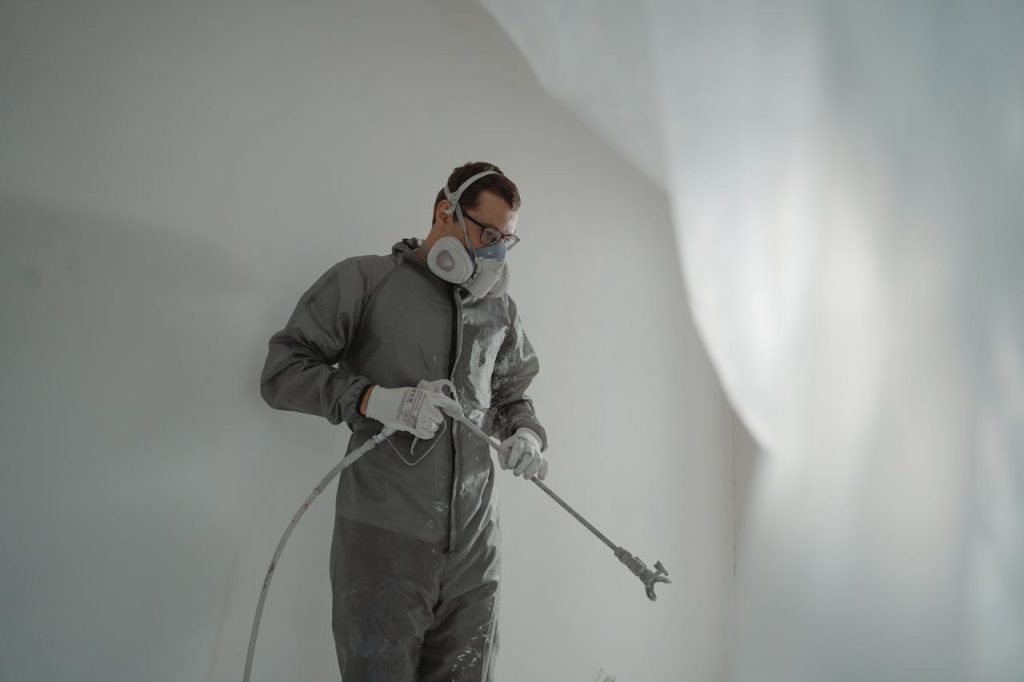a-man-in-gray-suit-painting-a-house-6474196 Person in protective gear painting a wall, showcasing house renovation work.